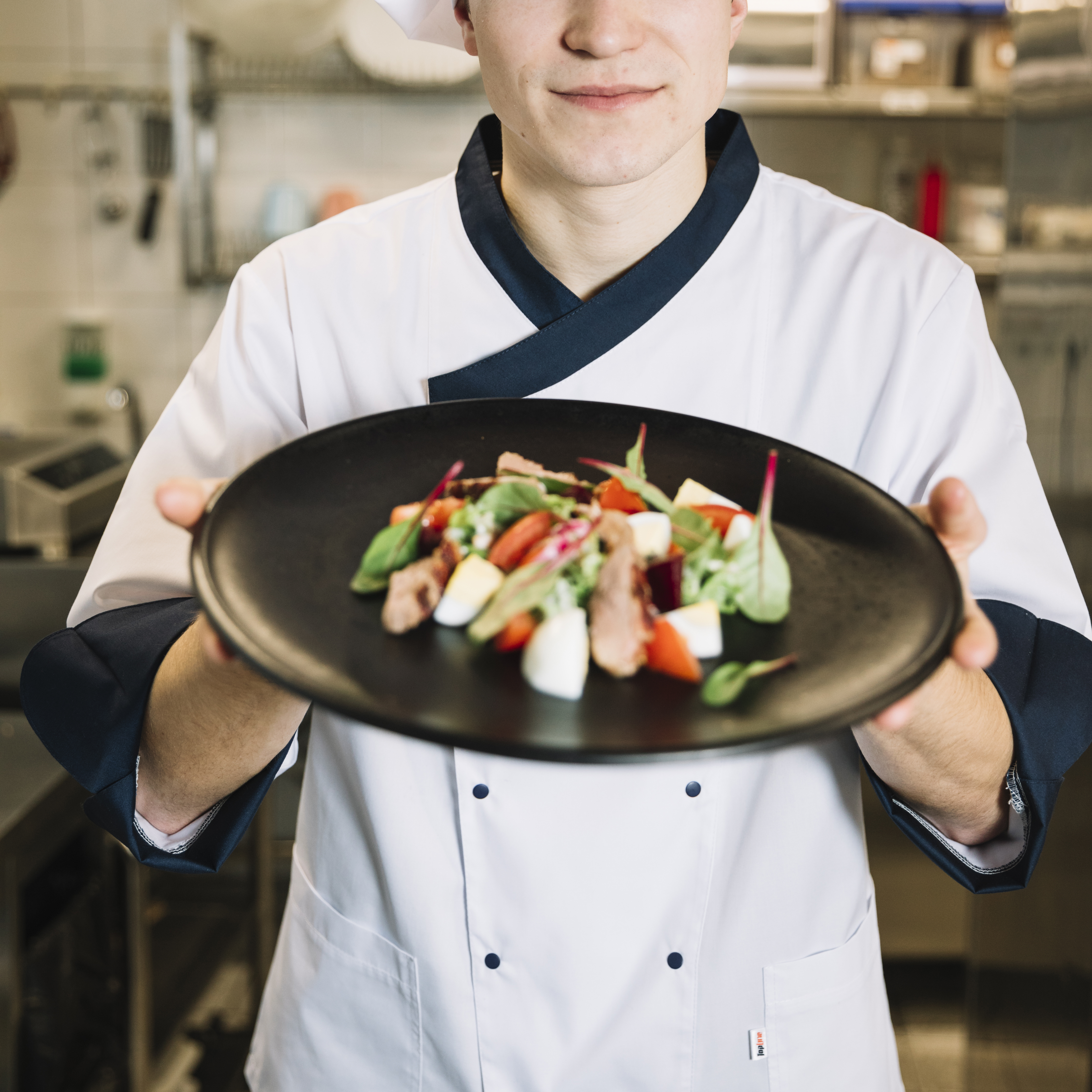 cook-holding-salad-with-meat-black-plate