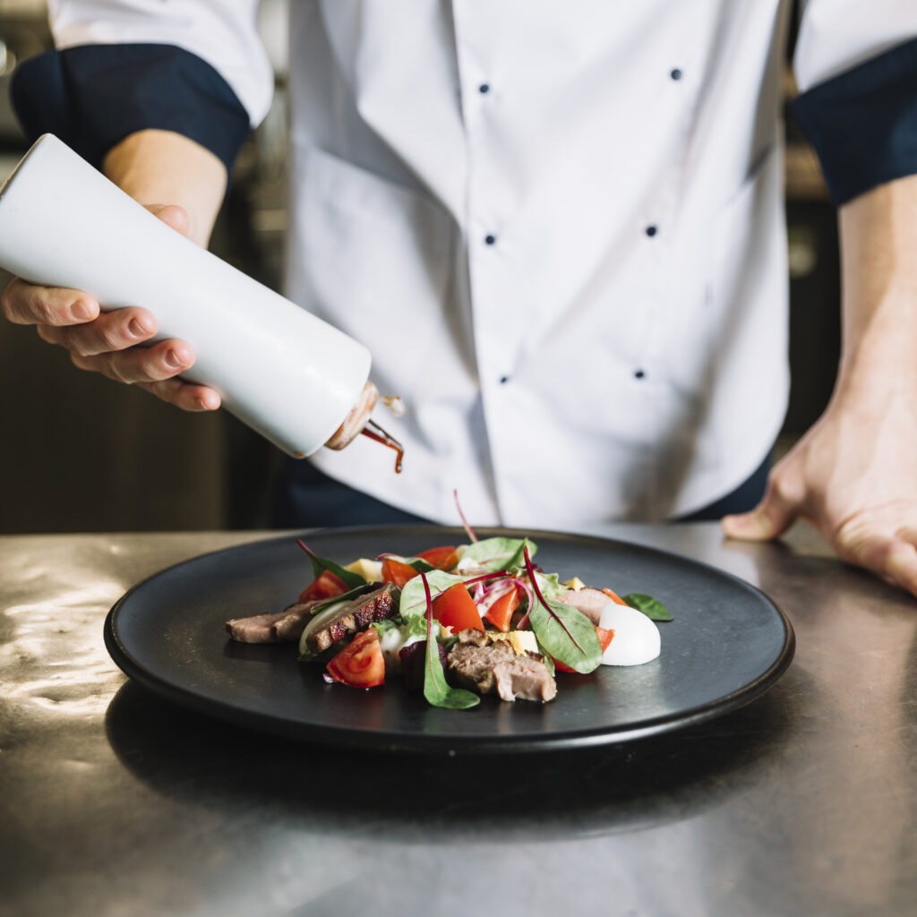cook-pouring-sauce-plate-with-salad